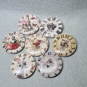 May include: Seven decorative wooden clock face buttons with various designs, including a clock tower, the Eiffel Tower, a crown, and floral patterns. The buttons are white with black numbers and accents.