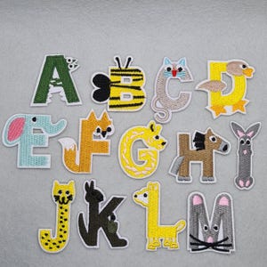 May include: Embroidered alphabet patches with animal designs. Letters A to M are shown, each incorporating an animal: bee, cat, duck, elephant, fox, giraffe, horse, and rabbit. Each patch has a white border and is set against a grey background.
