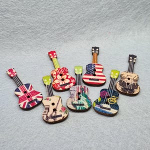 May include: Seven wooden guitar-shaped buttons with different colourful designs. The designs include a floral pattern, a US flag, a British flag, a musical note, a vintage travel poster, and a black and white design.
