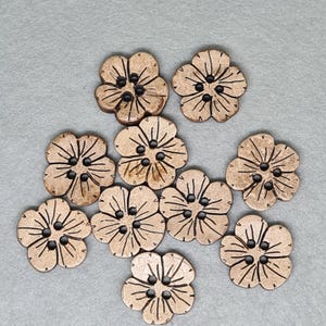 May include: A collection of ten flower-shaped buttons. The buttons are made of a light brown material with a natural wood grain appearance. Each button has four holes for sewing and a detailed petal design.