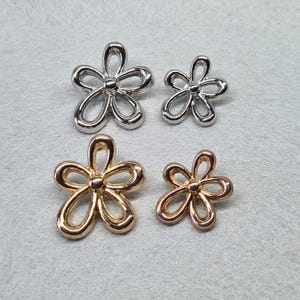 May include: Four metal flower charms, two silver and two gold. The charms are in the shape of a simple five-petal flower.