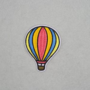 May include: A vibrant hot air balloon patch with a white outline. The balloon design includes yellow, blue, and pink vertical stripes, and a brown basket. This embroidered patch is suitable for customising garments or accessories.