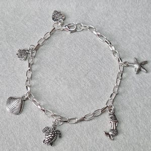 May include: Silver charm bracelet with a variety of sea-themed charms, including a seashell, starfish, turtle, and mermaid.