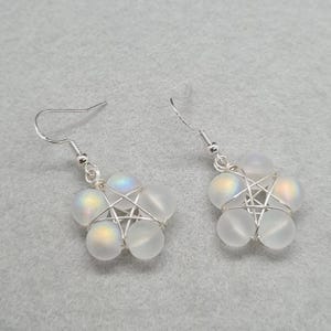 May include: A pair of dangle earrings featuring five frosted, iridescent white glass beads arranged in a star shape, secured with silver-toned wire wrapping. Each earring hangs from a simple silver-toned hook ear wire for pierced ears.
