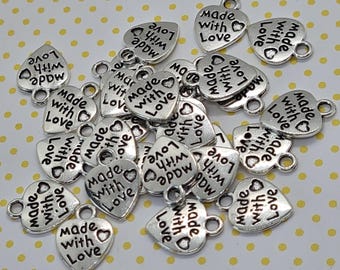 May include: A pile of silver heart-shaped charms with the words "Made with Love" on them. The charms have a small loop at the top for attaching to jewelry or other crafts.