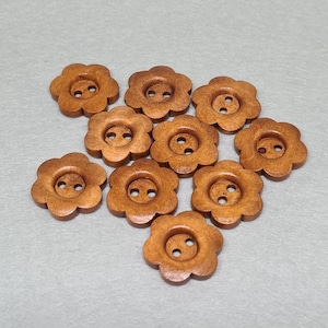 May include: A collection of ten wooden flower-shaped buttons. Each button has a light brown color with a two-hole design in the center. The buttons are arranged on a light gray surface.