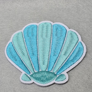 May include: An embroidered seashell patch in shades of blue and green. The seashell is a popular design for nautical and beach-themed crafts.
