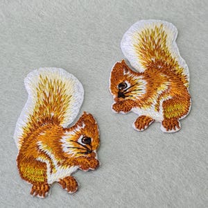May include: Two embroidered iron-on patches of squirrels with white fluffy tails and brown bodies.