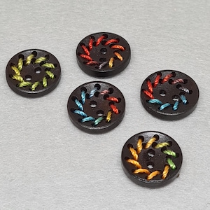May include: Five dark brown wooden buttons with colorful embroidered thread accents. Each button features a circular design with various colors of thread, including yellow, orange, red, blue, and green, stitched around the edges.