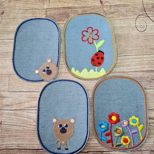 May include: Four oval-shaped denim patches with embroidered designs. Two patches feature a brown bear with black eyes. One patch features a red flower with a ladybug on a green stem. The last patch features a cluster of colorful flowers with green stems.