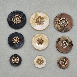 May include: Nine round buttons in different sizes and shades. Each button has a gold-coloured cross design within a rope-like border. The colours include black, cream, and brown with marbled patterns. Ideal for sewing and craft projects.