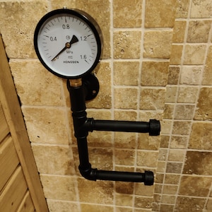 May include: Black industrial pipe towel holder with a round pressure gauge attached to the wall. The gauge has a white face with black markings and the text "HONGSEN" and "MPa".
