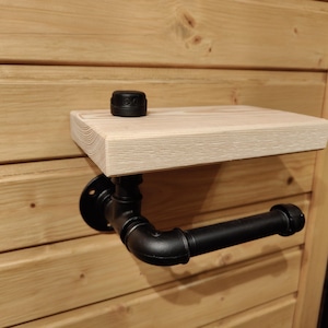 May include: A wooden shelf with black metal pipe supports. The shelf is mounted to a wall and has a black cap on the top.