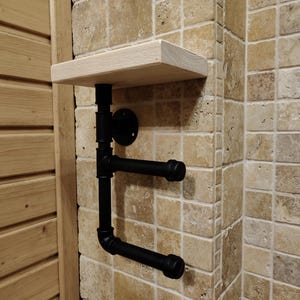 May include: A black metal pipe shelf with a wooden top shelf. The shelf is mounted on a tiled wall.