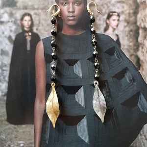 May include: A pair of long, dangling earrings with black beads and a leaf-shaped charm at the bottom. One charm is gold and the other is silver.