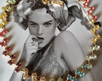 Può includere: Una collana a catena dorata con un gradiente arcobaleno di strass colorati. La collana è realizzata con piccoli strass ovali incastonati in una montatura in metallo dorato.
