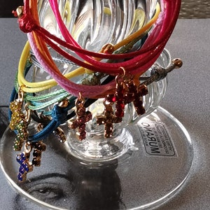 May include: A set of colorful string bracelets with cross charms. Each charm is decorated with colorful rhinestones. The bracelets are displayed on a clear glass stand.