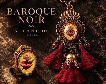 May include: A gold-toned necklace and ring set featuring oval cameos with a red heart and sword motif. The necklace has a flame-shaped top, red crystal accents, and three deep red tassels. Text reads BAROQUE NOIR ATLANTIDE GIOIELLI.