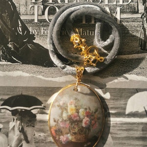 May include: A gray velvet choker necklace with a gold pendant featuring a painted oval cameo of a bouquet of flowers in a basket.