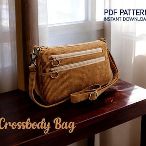 Op de afbeelding: Een goudbruine corduroy crossbody tas met twee vakken met ritssluiting en ringtrekkers. Het heeft een voorvak en een verstelbare riem. De tekst "Crossbody Bag" wordt in cursief weergegeven. De tekst "PDF Pattern Instant Download" is ook zichtbaar.