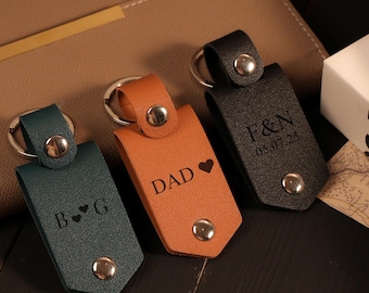 May include: Three leather keychains in teal, orange, and black. Each keychain has a silver-colored metal ring and snap closure. The teal keychain has "B ♥ G" engraved, the orange one says "DAD ♥", and the black one says "F&N 05.07.25".