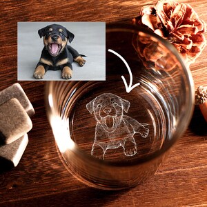May include: A clear rocks glass with a detailed etched image of a Rottweiler puppy. The glass is on a wooden surface, with a pine cone and a small acorn visible. The puppy is black and tan.