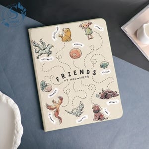 May include: A beige notebook with the words "FRIENDS at Hogwarts" and illustrations of various creatures. The cover features a pegasus, a phoenix, a dog, and other whimsical characters.