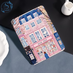 May include: A tablet case with a pink and blue illustration of a bookstore. The case features a pink facade with the words "BOOK SHOP" above the storefront. The design includes windows, a person, and a tree, with a blue sky.