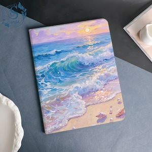 May include: A notebook featuring a beach scene cover. The artwork shows ocean waves, a sandy shore, seashells, and a sunset in shades of blue, purple, and yellow. The notebook is on a grey surface.