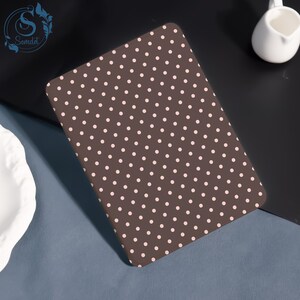 May include: A brown rectangular item featuring a pattern of small, evenly spaced, pale pink polka dots. The item is angled, and the polka dots are consistent in size and shape. It appears to be a cover or mat, possibly for a desk or table.
