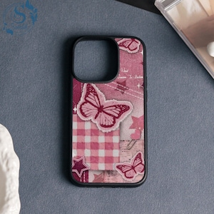 Könnte beinhalten: Eine rosa Handyhülle mit schwarzem Rand mit einem Schmetterlingsdesign. Die Hülle hat ein Patchwork-Design mit Schmetterlingen, Sternen und einem Vichy-Muster. Der Text "Need Dreams To Believe" ist sichtbar.