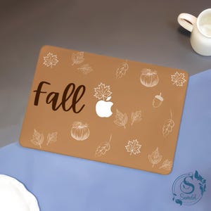 May include: A brown laptop skin with the word "Fall" in a script font. The skin is decorated with white leaf and pumpkin illustrations, and a white apple logo. The design has a fall theme.