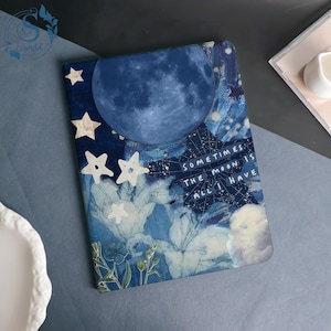 May include: A notebook with a celestial design in shades of blue and white, featuring a large moon, stars, and floral elements. The cover includes the text "Sometimes the moon is all I have". The notebook is rectangular.