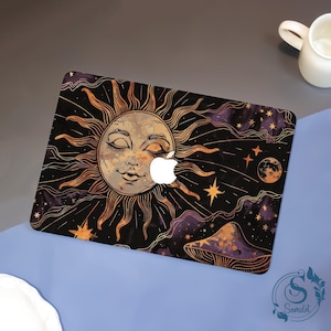 Op de afbeelding: Een laptop skin met een hemels ontwerp. Het heeft een zonnegelaat, sterren en een paddenstoel in goud-, oranje- en paarse tinten tegen een zwarte achtergrond. Het Apple-logo is zichtbaar.