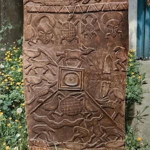 Könnte beinhalten: Ein verwittertes, rechteckiges Holzpaneel mit geschnitzter Reliefkunst. Das braune Paneel zeigt verschiedene Tiere, menschliche Gesichter und geometrische Formen. Das Kunstwerk hat ein rustikales, gealtertes Aussehen, was darauf hindeutet, dass es sich um ein antikes oder Vintage-Stück handelt.