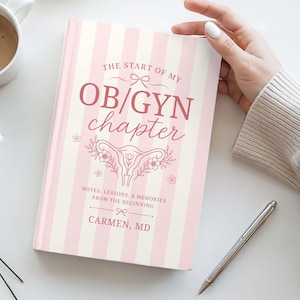 May include: A pink and white striped journal titled "The Start of My OB/GYN Chapter" with floral illustrations. A cup of coffee, a pen, and flowers are also present. The journal's cover includes the name "Carmen, MD".