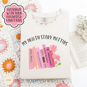 Puede incluir: Camiseta de color marfil con el texto "MY HEALTH STORY MATTERS" y un gráfico de libros rosas etiquetados con afecciones médicas. La camiseta también presenta el texto "CUSTOMIZE WITH YOUR DIAGNOSES & CONDITIONS!"