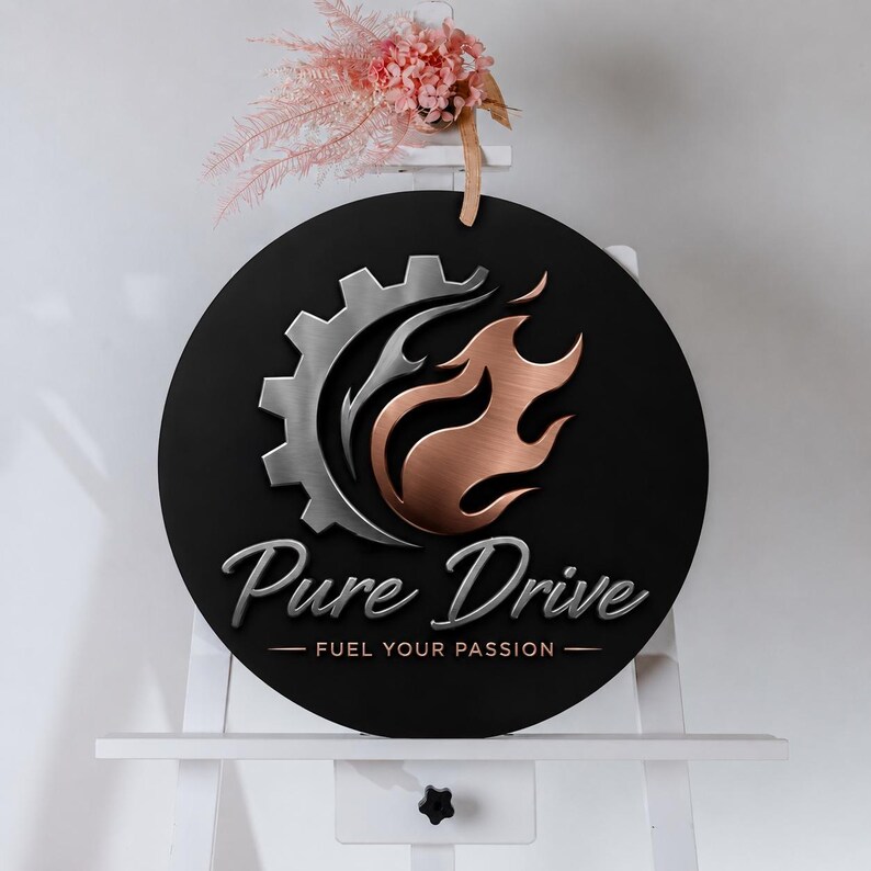 May include: A round black sign with the words "Pure Drive" in a cursive font, and "FUEL YOUR PASSION" below. The sign features a silver gear and copper-colored flames. The sign is displayed on a white easel.
