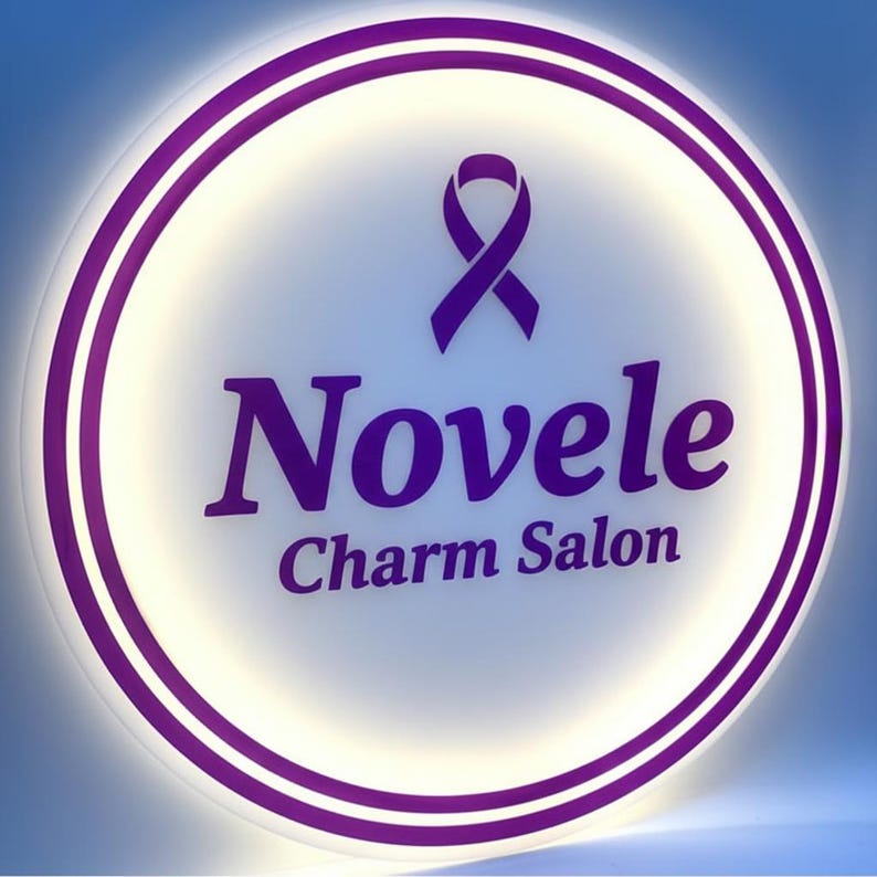 K&ouml;nnte beinhalten: Rundes, beleuchtetes Schild mit einer lila Schleife und dem Schriftzug "Novele Charm Salon" in Lila. Das Schild hat eine wei&szlig;e Mitte, einen lila Rand und einen blauen Farbverlauf im Hintergrund.