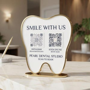 May include: A tooth-shaped sign with a gold frame and white face. The text reads SMILE WITH US, PEARL DENTAL STUDIO, SCAN TO BOOK, and includes two QR codes labeled INSTAGRAM @pearldentalstudio and BOOK ONLINE BOOK NOW, all on a flat base.