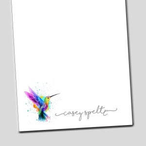 May include: A watercolor illustration of a colorful hummingbird with a splash of paint behind it. The name "casey speltz" is written in cursive at the bottom of the image.
