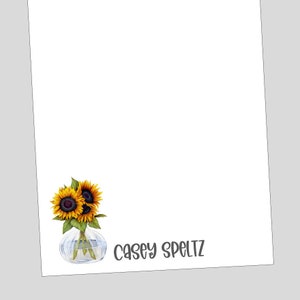 May include: A white notepad with a sunflower bouquet in a clear glass vase. The name "Casey Speltz" is written in gray cursive at the bottom of the notepad.