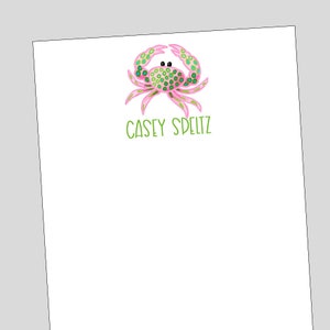 May include: A white notepad with a pink and green crab illustration and the name "Casey Speltz" written in green.