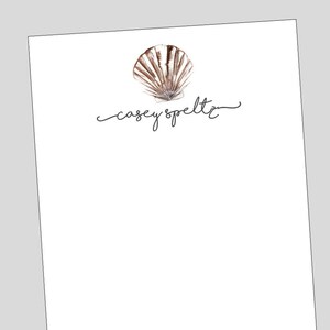 May include: A white notepad with a brown seashell illustration and the text "casey speltz" in cursive.