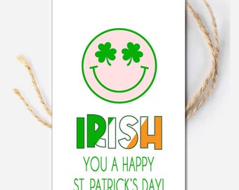May include: A white card with a pink smiley face with green shamrocks for eyes. The text "IRISH" is in green, white, and orange letters, with the white letter "I" having a green shamrock on it. The text "YOU A HAPPY ST. PATRICK'S DAY!" is below the word "IRISH".