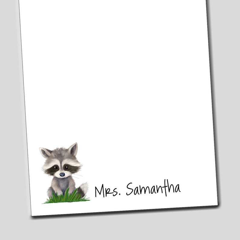 May include: A white notepad with a cute cartoon raccoon illustration and the text "Mrs. Samantha" at the bottom.