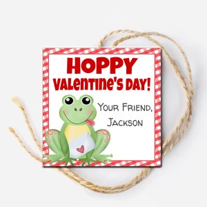 May include: A red and white checkered border surrounds a white card with the text "Hoppy Valentine's Day!" in red. A green frog with a red heart on its belly holds a yellow envelope with a red heart on it. The text "Your Friend, Jackson" is below the frog.