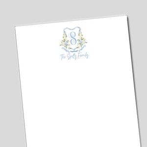 May include: White stationery with a light blue floral crest design. The crest features the letter "S" and the words "The Spettz Family" in a delicate script. The design includes light blue ribbons and floral accents.