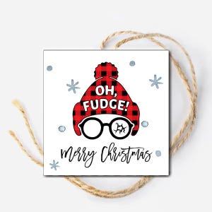 May include: A white Christmas gift tag with a red and black plaid hat with a white pom pom and the text "Oh, Fudge!" and black framed glasses with a crack in one lens. The tag also has the text "Merry Christmas" in black cursive writing and silver snowflakes.