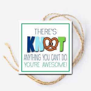 Può includere: Un biglietto bianco con bordi verdi, blu e azzurro. Il biglietto ha il testo "There's Knot Anything You Can't Do You're Awesome!" con un pretzel al centro della parola "Knot".